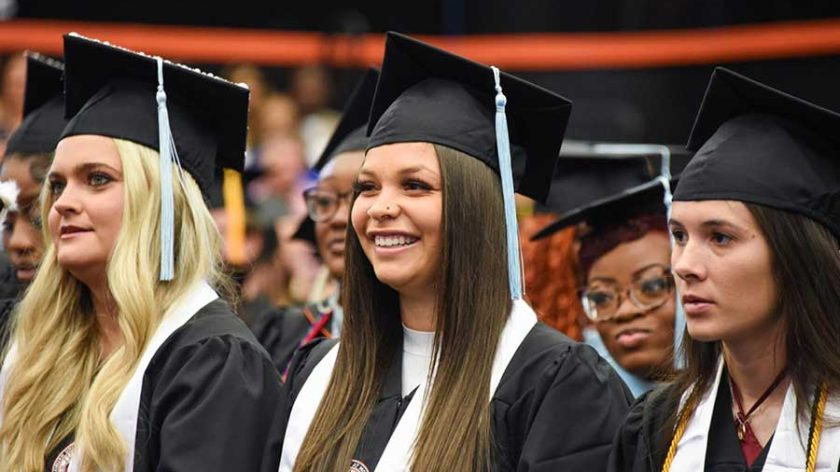 Auburn University At Montgomery Graduates In Caps And Gowns Smiling During Commencement Ceremony.