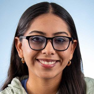 A smiling person wearing glasses, showcasing a friendly expression against a light background.