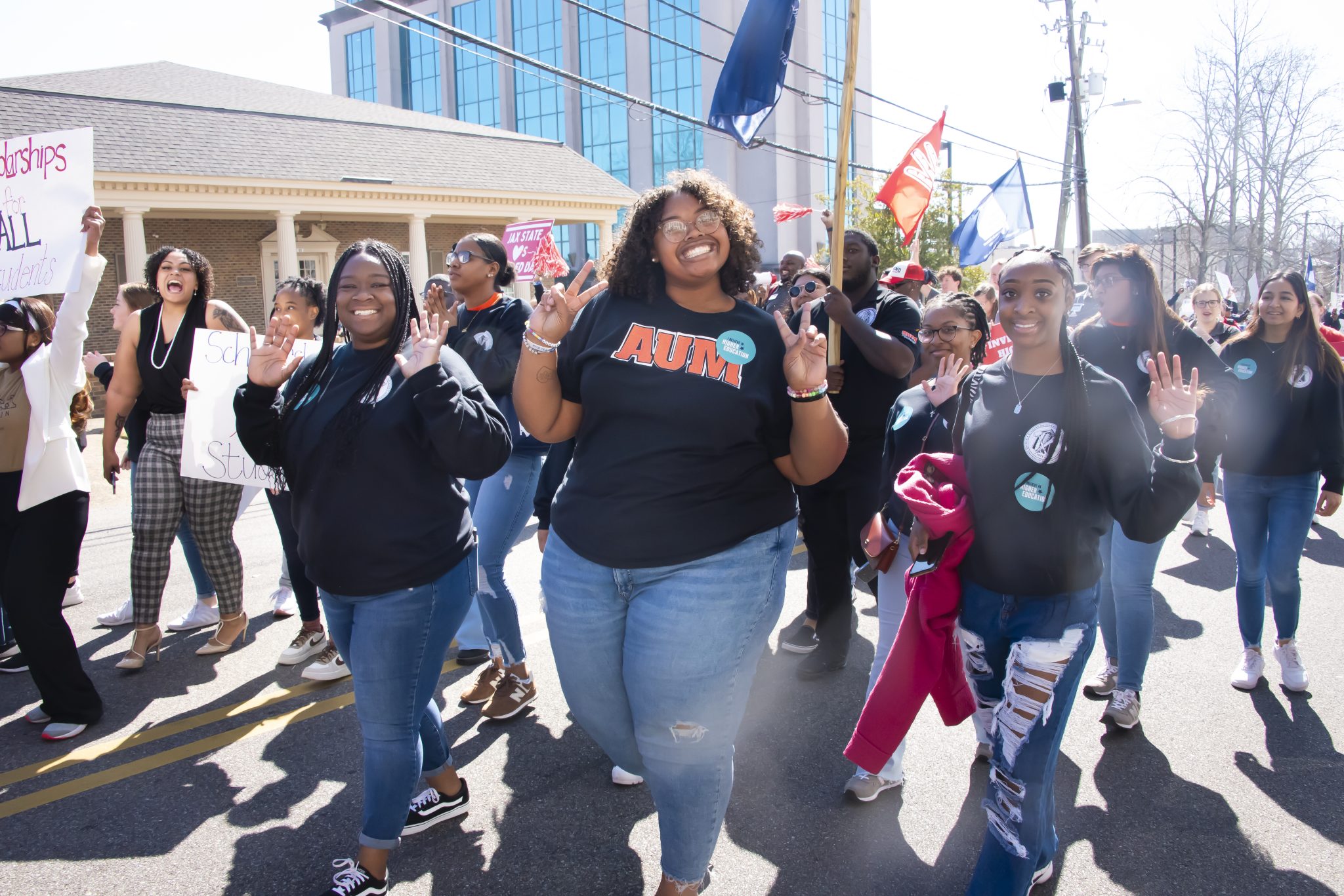 Auburn University at Montgomery students march downtown, smiling in AUM shirts and holding signs during a campus parade