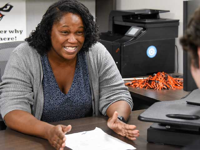 Auburn University at Montgomery advisor meets with a student in an office, discussing paperwork at a desk.
