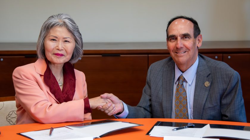 Auburn University At Montgomery Leaders Shake Hands While Signing Partnership Documents At A Meeting Table.