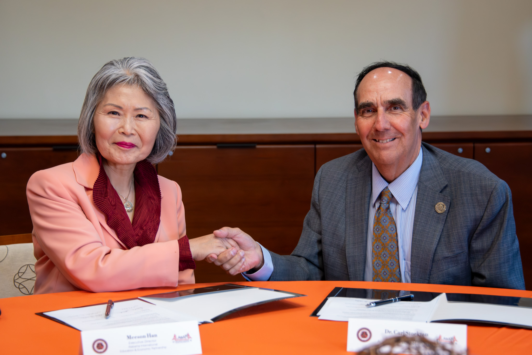Auburn University at Montgomery leaders shake hands while signing partnership documents at a meeting table.