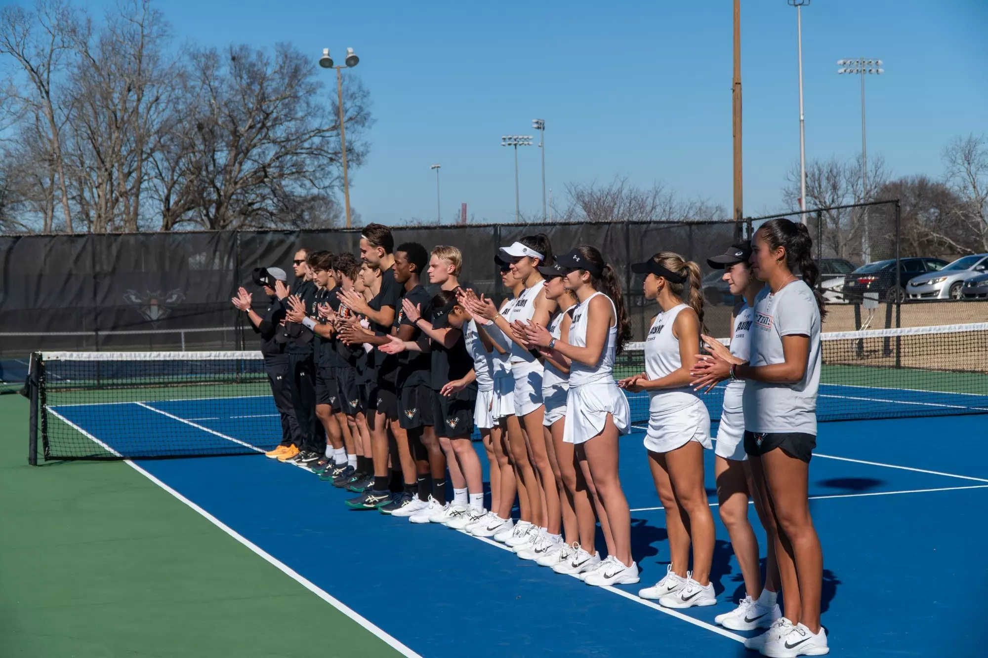 Auburn University at Montgomery tennis players line up clapping on outdoor blue courts before a match.