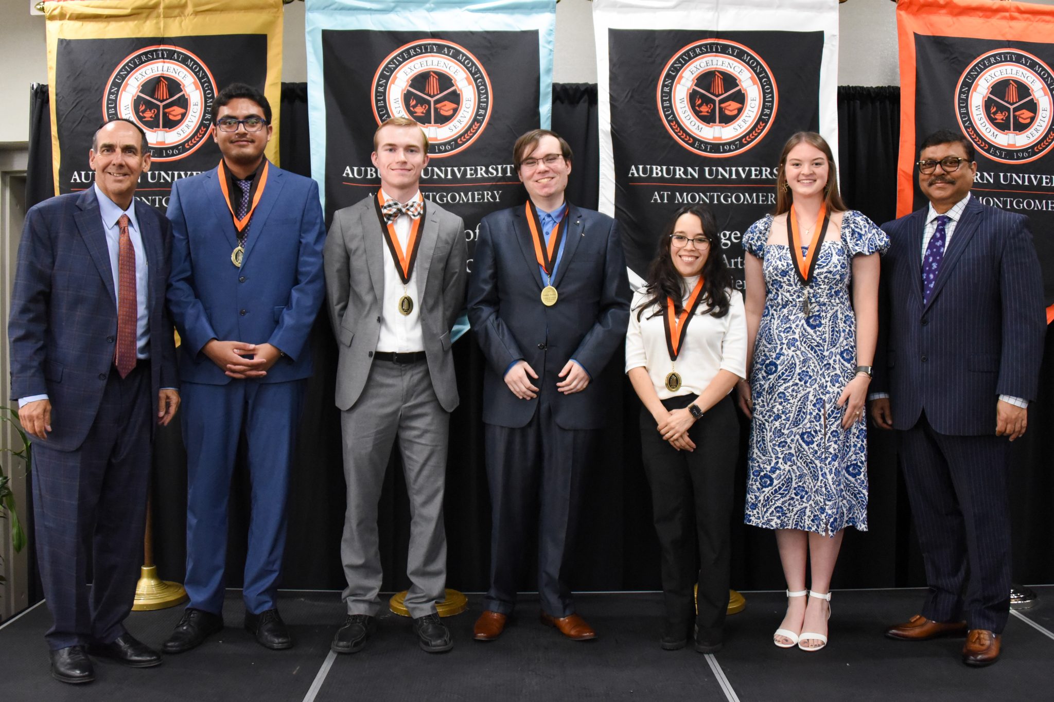 Auburn University at Montgomery honors ceremony with students wearing medals and administrators on stage before AUM banners