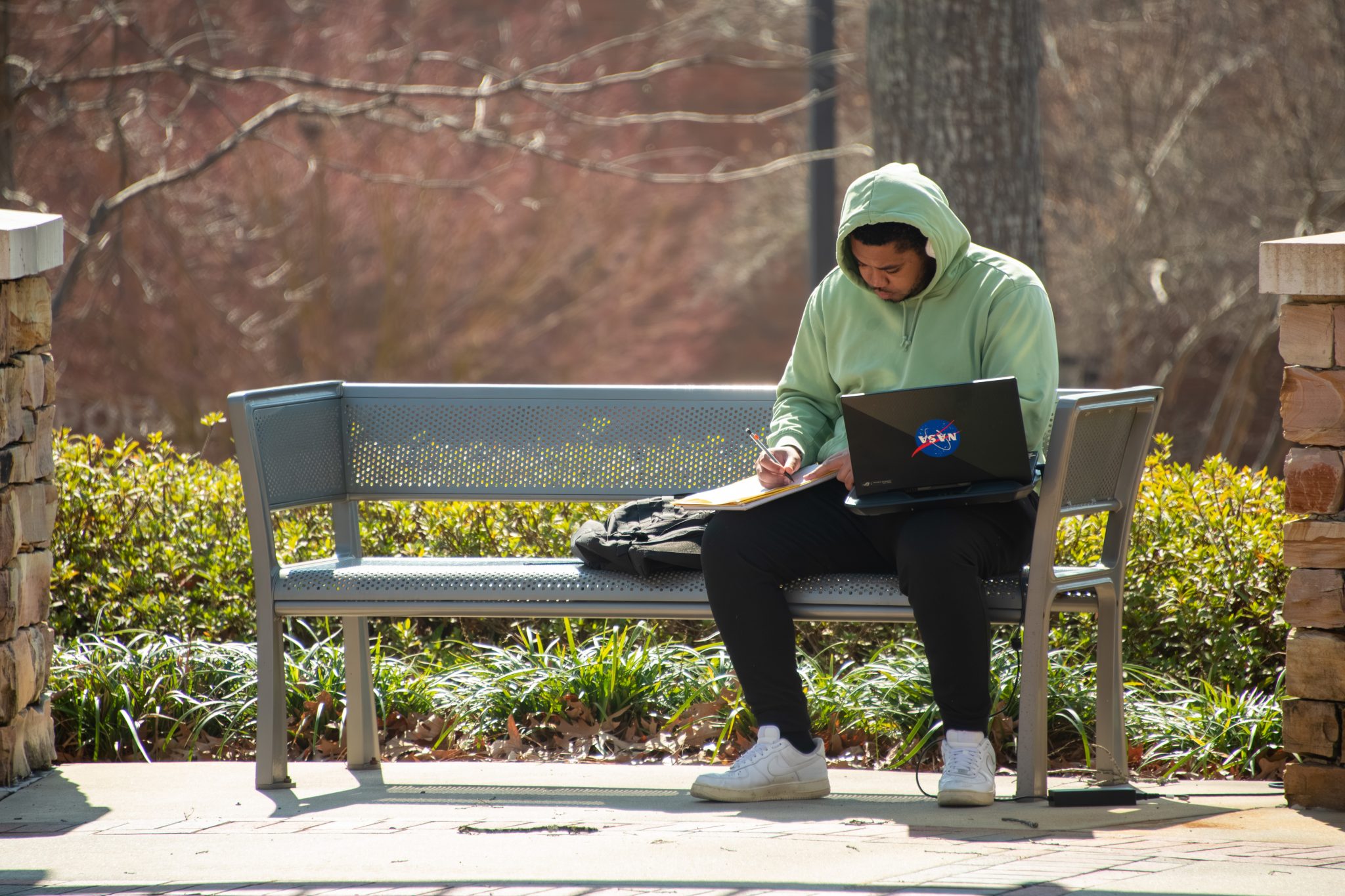 AUM student studying on a bench in The Grove with a laptop and notebook.