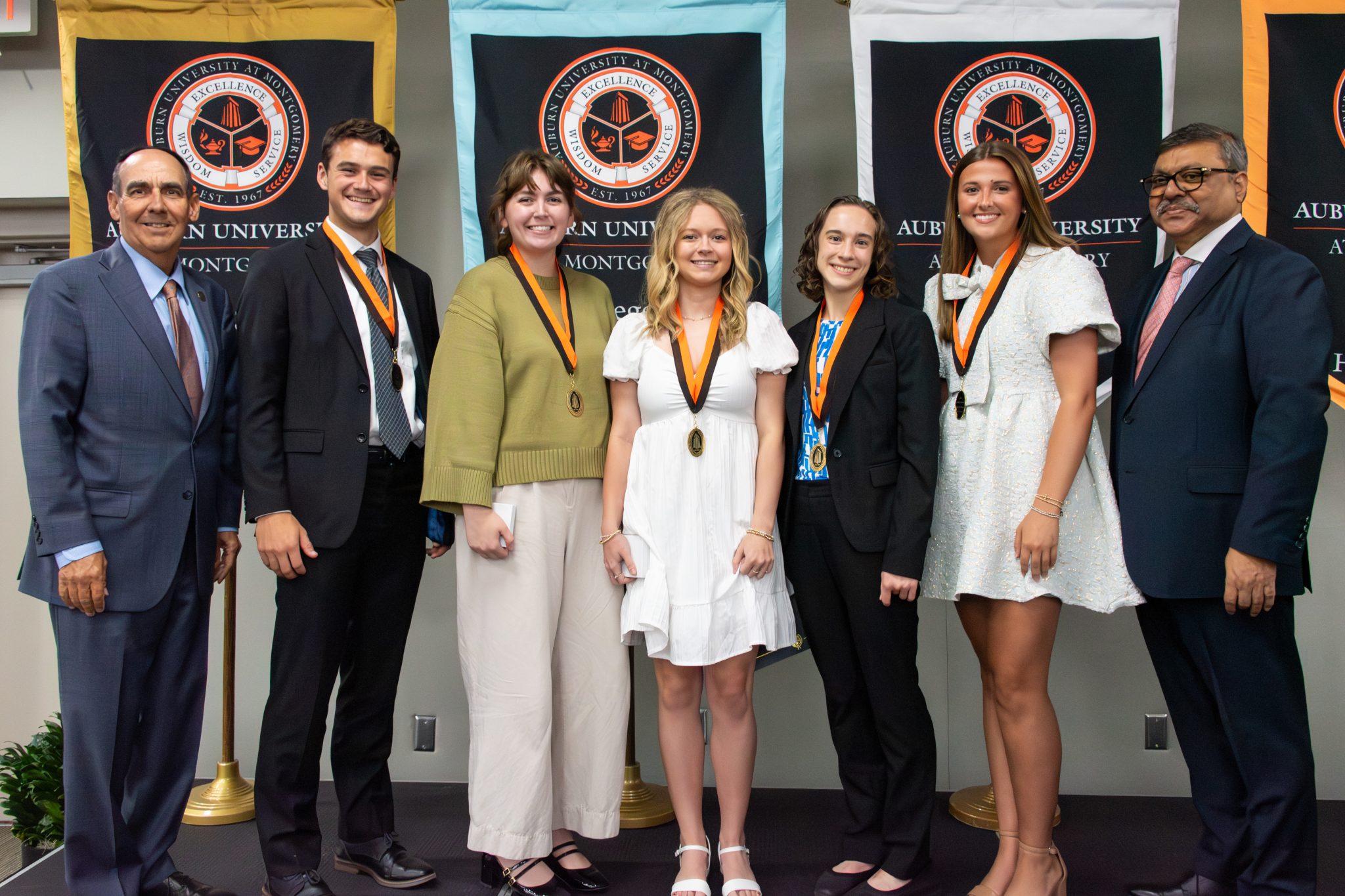 Auburn University at Montgomery honors ceremony: students wearing medals pose with administration before AUM banners.
