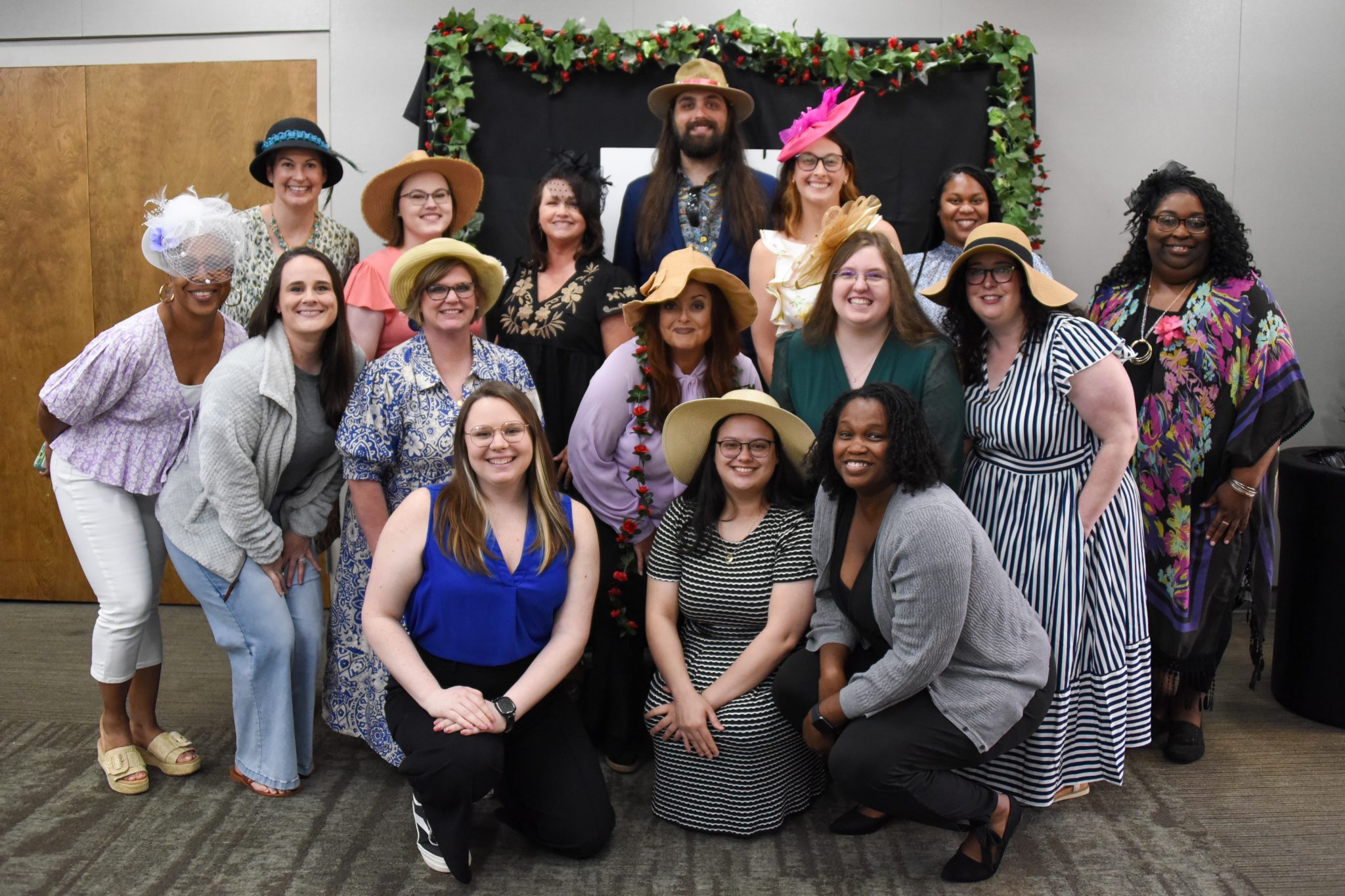 Group photo of Auburn University at Montgomery staff in stylish hats at a campus event, smiling by a decorated backdrop.