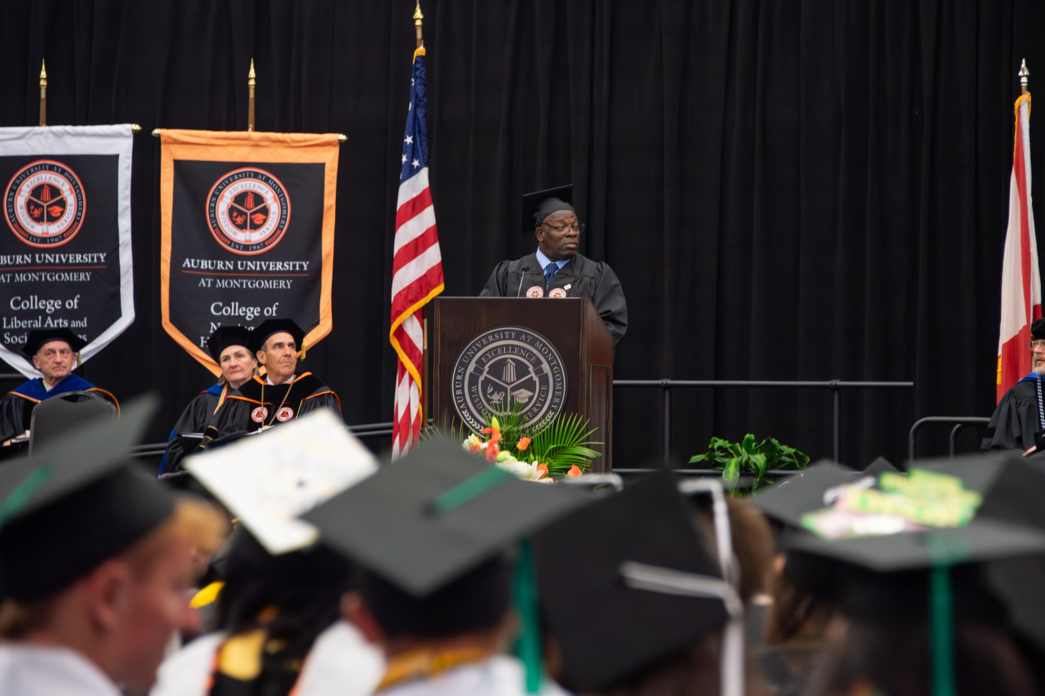 AUM commencement speaker at podium with Auburn University at Montgomery banners, addressing graduates