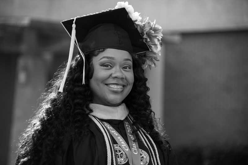 AUM graduate with honor cords smiles in cap and gown at Auburn University at Montgomery commencement.