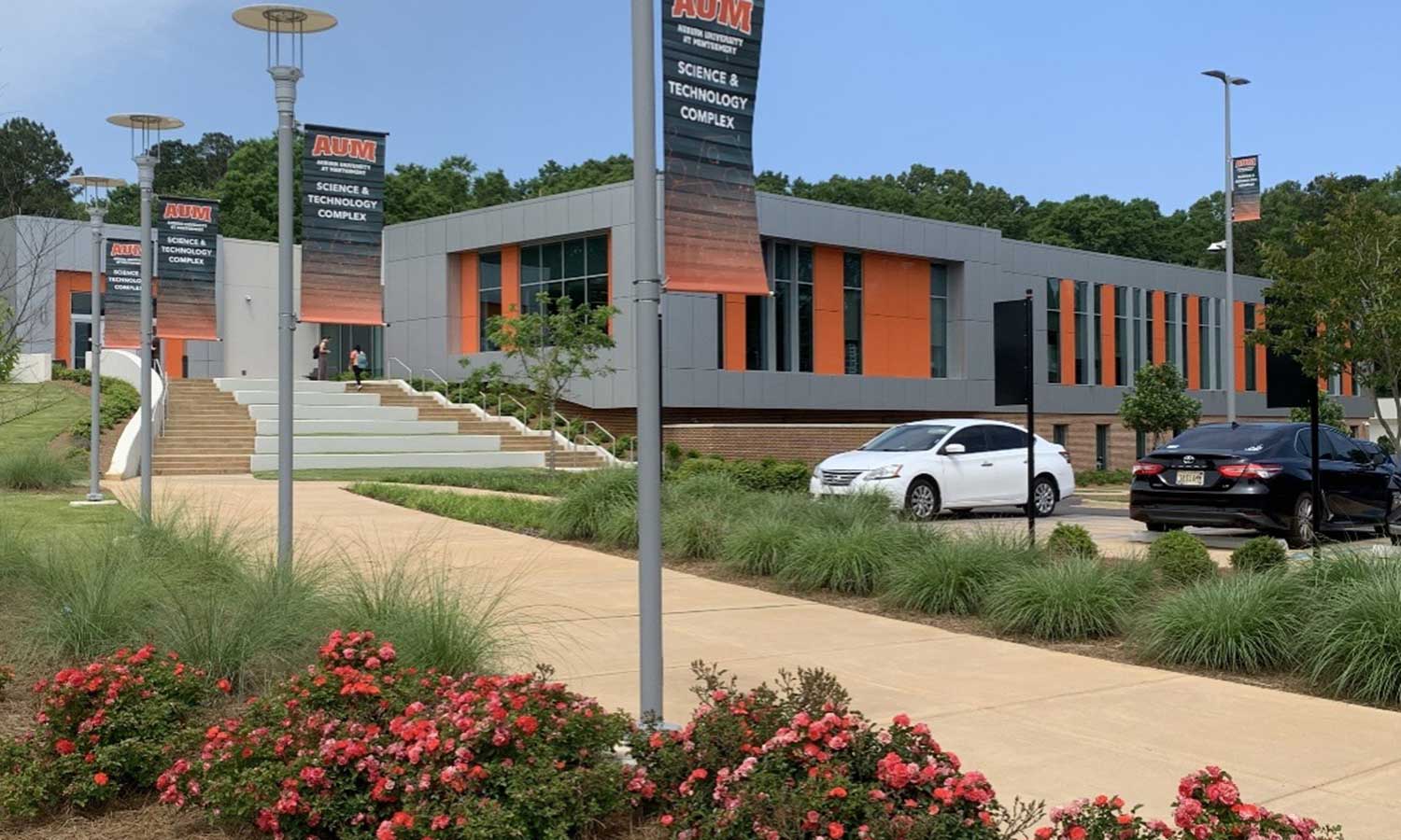 Exterior of Auburn University at Montgomery Science & Technology Complex with banners, flowers, and students on campus