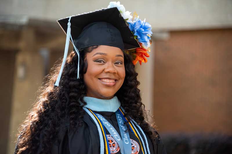 Auburn University at Montgomery graduate smiles in cap and gown with honor cords and flowered mortarboard