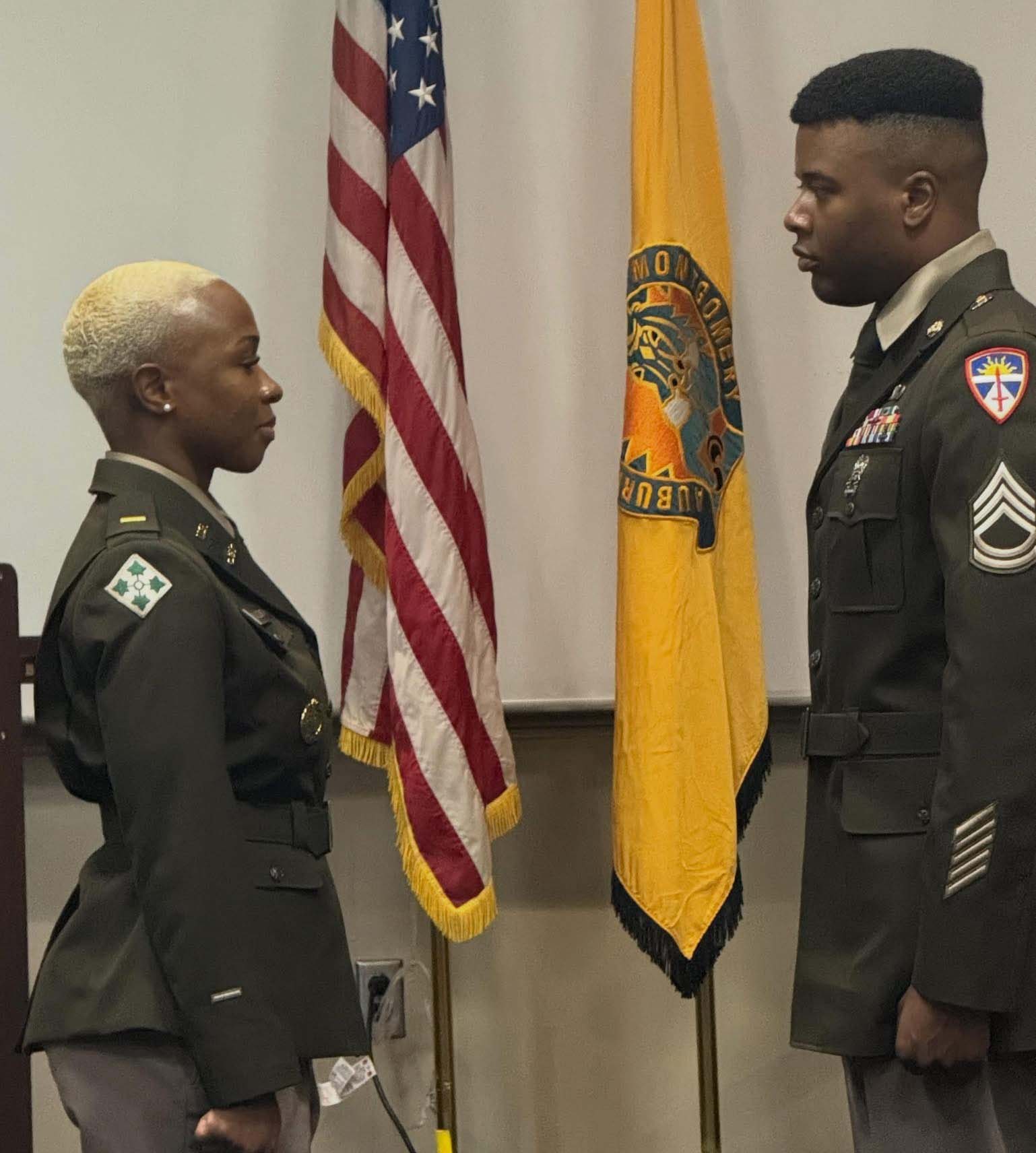 Auburn University at Montgomery ROTC ceremony: two cadets in uniform face each other before U.S. and unit flags
