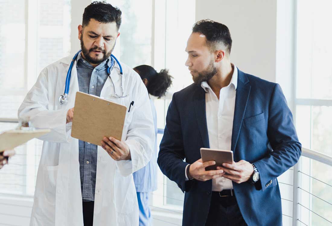 Auburn University at Montgomery doctor reviews a clipboard with a business professional holding a tablet in a bright hallway