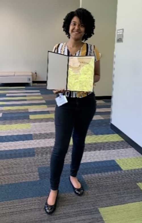 Auburn University at Montgomery woman displays award certificate in modern campus hallway