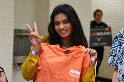 AUM student flashes peace sign while holding Auburn University at Montgomery T-shirt during campus orientation event.
