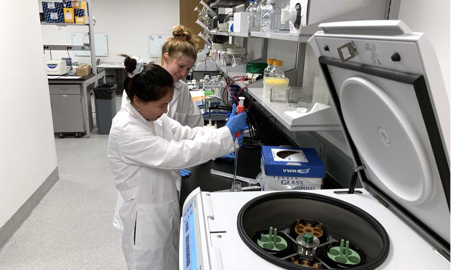 Auburn University at Montgomery students use a pipette beside a centrifuge during biology research in a lab.