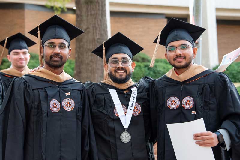 Auburn University at Montgomery graduates in caps and gowns smile during AUM commencement on campus.