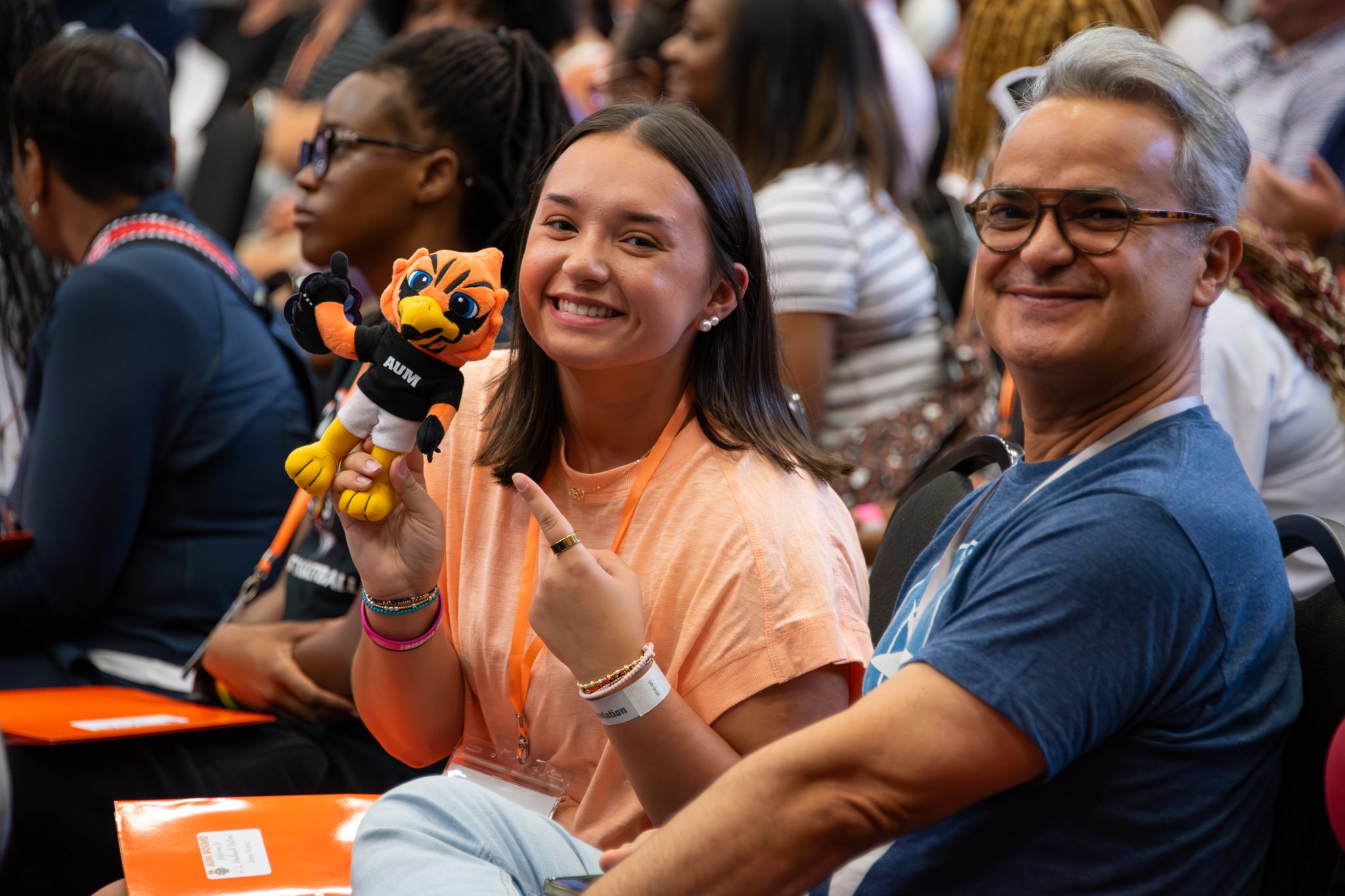 AUM student holding Warhawks mascot plush at Auburn University at Montgomery orientation, smiling with a supporter in crowd.