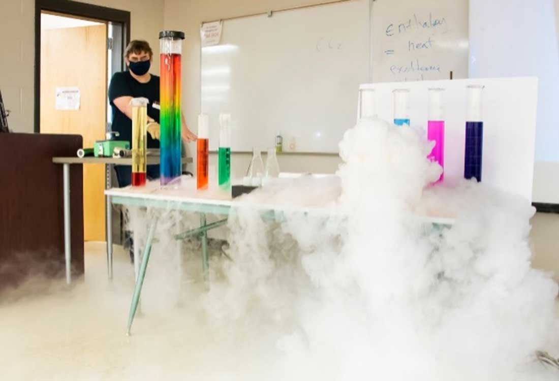 Auburn University at Montgomery chemistry demo: a person with colorful test tubes and dry ice fog in a campus lab classroom