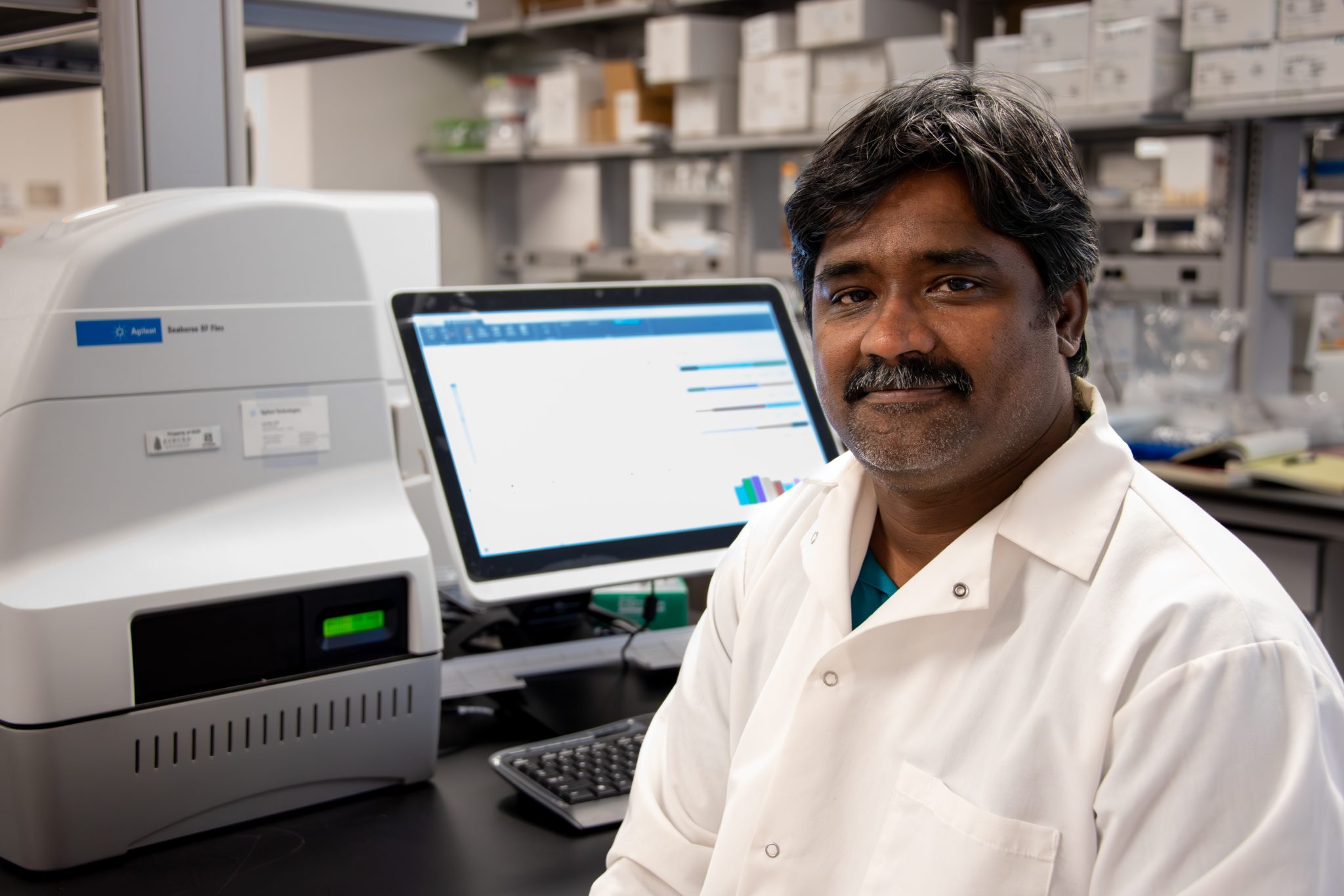Auburn University at Montgomery researcher in lab coat at computer and Agilent Seahorse XF analyzer in biology lab