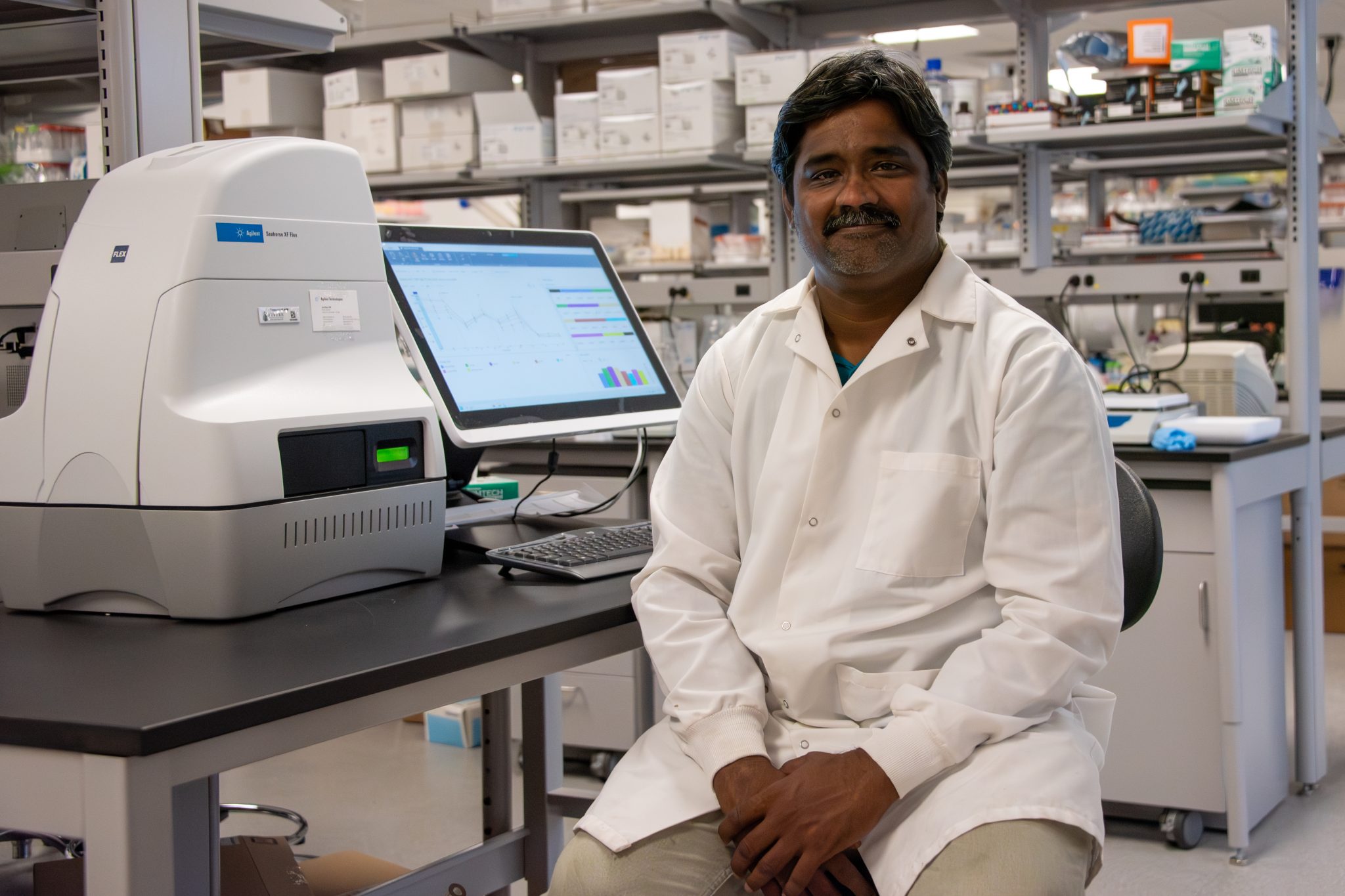 Siva Sakamuri, assistant professor of chemistry in Auburn University at Montgomery’s College of Sciences, stands beside the Seahorse XFe24 Metabolic Flux Analyzer in his laboratory in AUM’s Science and Technology Complex. The instrument, acquired through a National Institutes of Health grant, will support research into how cellular energy production influences brain health, aging and disease. Photo by Nicolette Parrish / AUM.