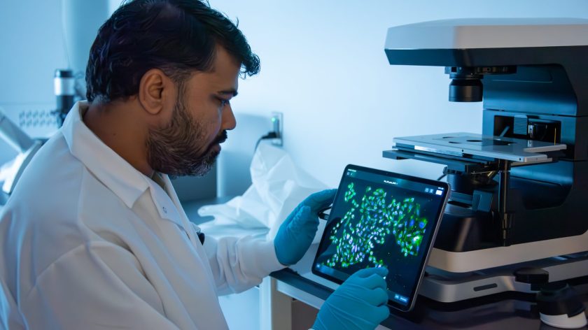 Auburn University At Montgomery Researcher Analyzes Fluorescent Cell Images On Tablet Beside Microscope In Lab