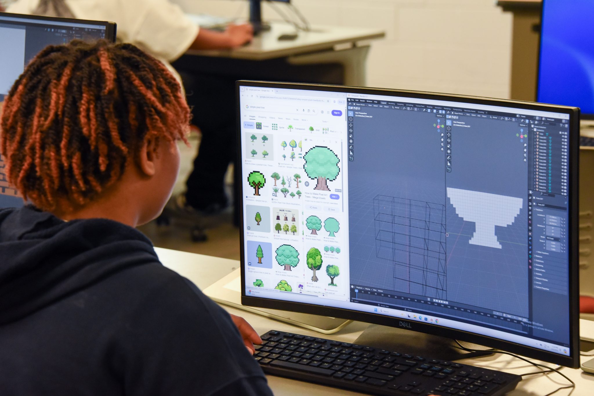 Middle school student creates 3D model in computer lab using Blender and pixel art references during AUM's animation summer camp.
