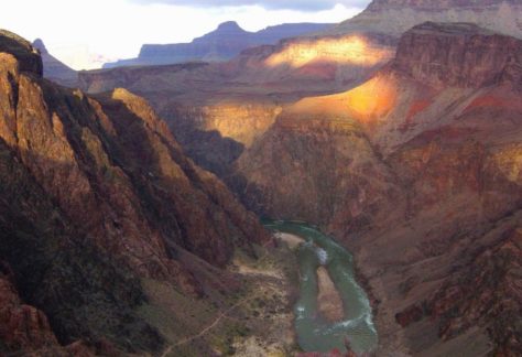 Grand Canyon at sunset with the Colorado River winding between steep cliffs and layered rock formations.