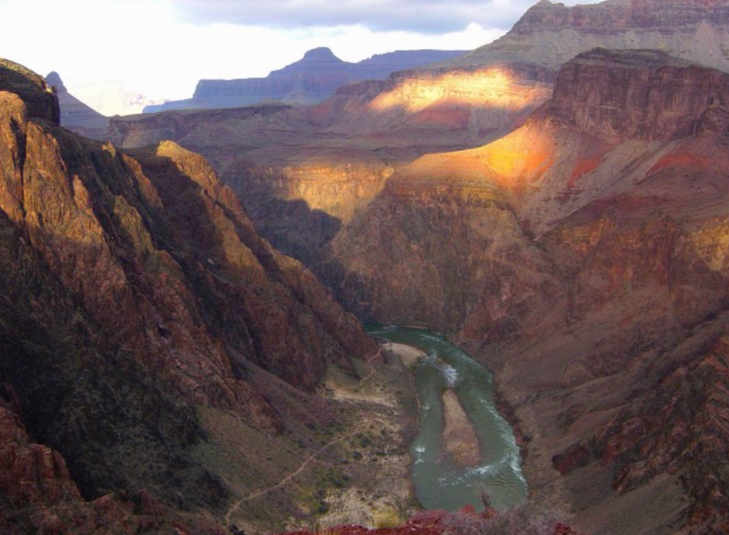 Grand Canyon at sunset with the Colorado River winding between steep cliffs and layered rock formations.