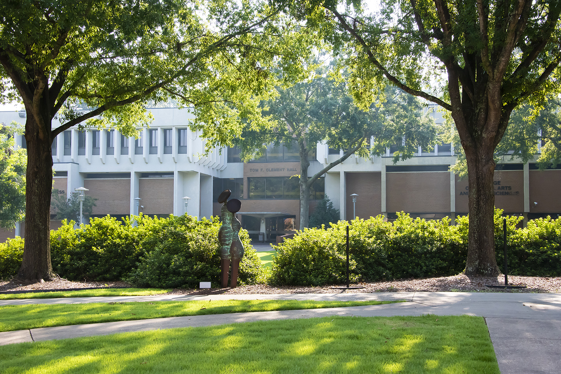 Tom F. Clement Hall at Auburn University at Montgomery framed by trees, sculpture, and green lawn on a sunny day
