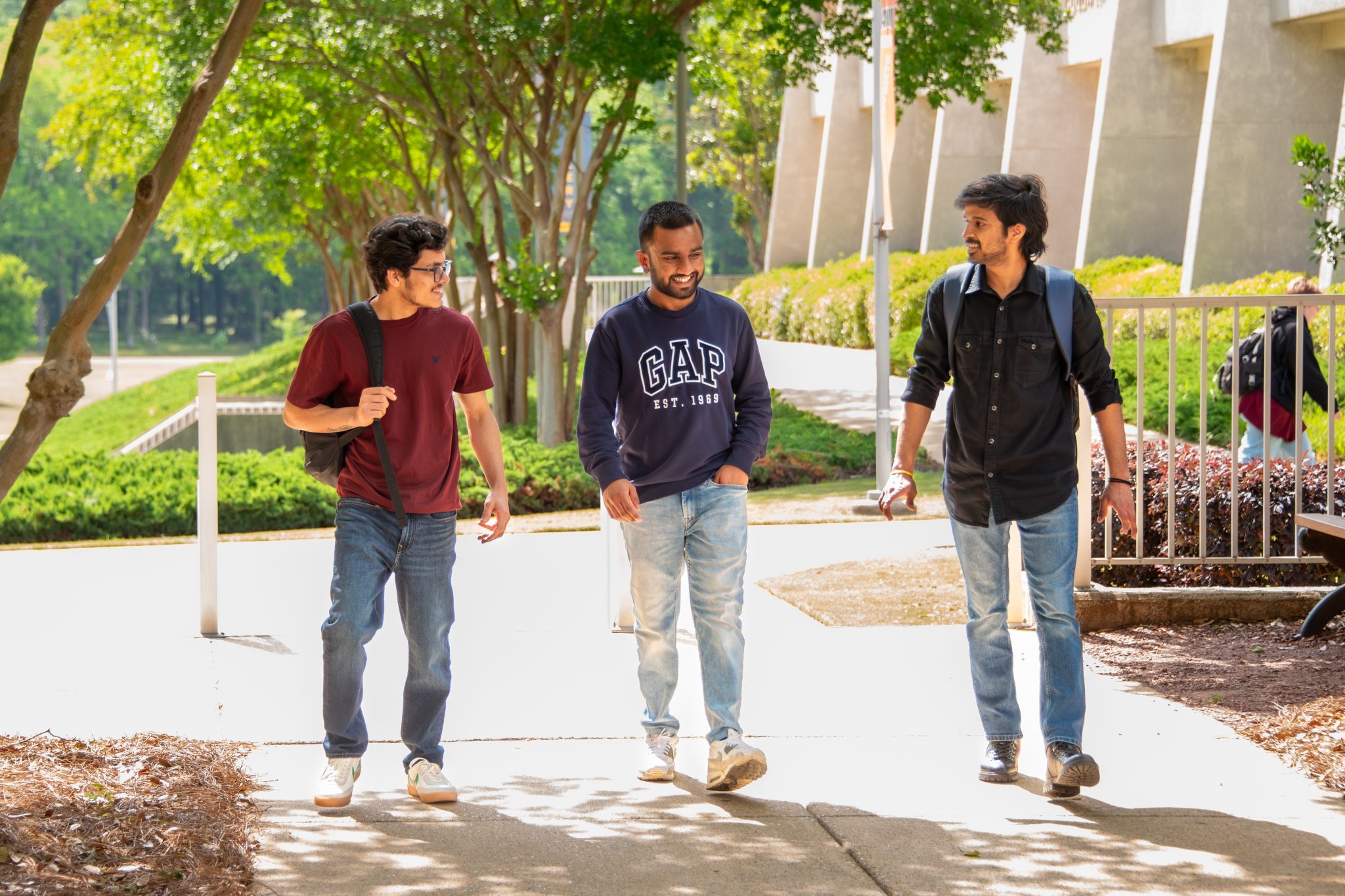 Three Auburn University at Montgomery students walking together on a sunny campus path with backpacks.
