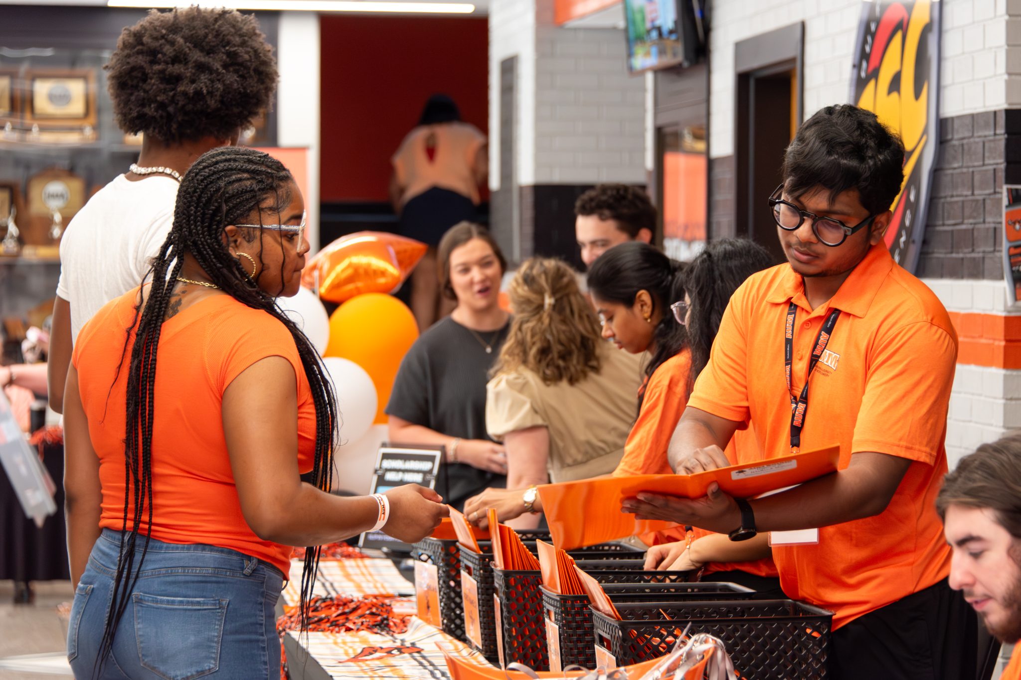 Auburn University at Montgomery students hand out orange welcome packets at campus orientation check-in table.