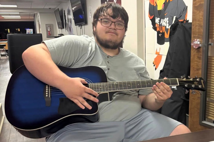 Auburn University at Montgomery student playing blue acoustic guitar in campus lounge