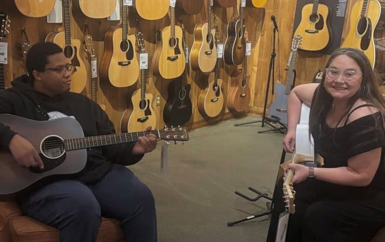 Auburn University At Montgomery Students Play Acoustic Guitars In A Shop With A Wall Of Guitars.