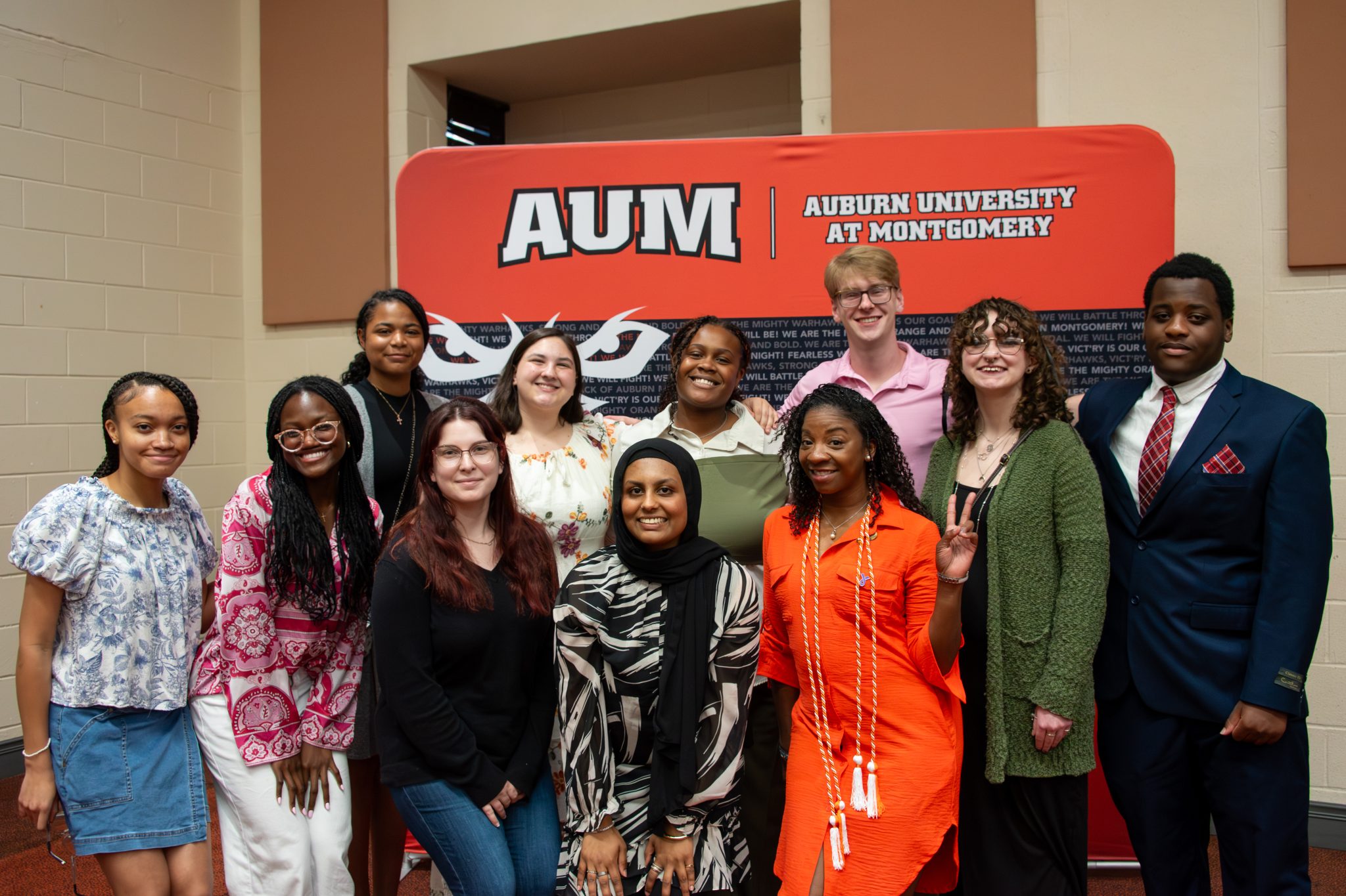 Auburn University at Montgomery honors students smile together at an Honors Graduation, posing in front of a campus backdrop.