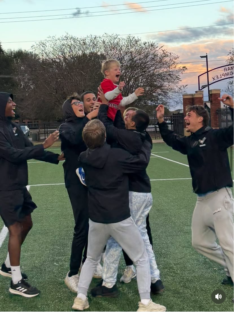 Auburn University at Montgomery students lift a smiling child on the soccer field during a campus celebration at sunset.