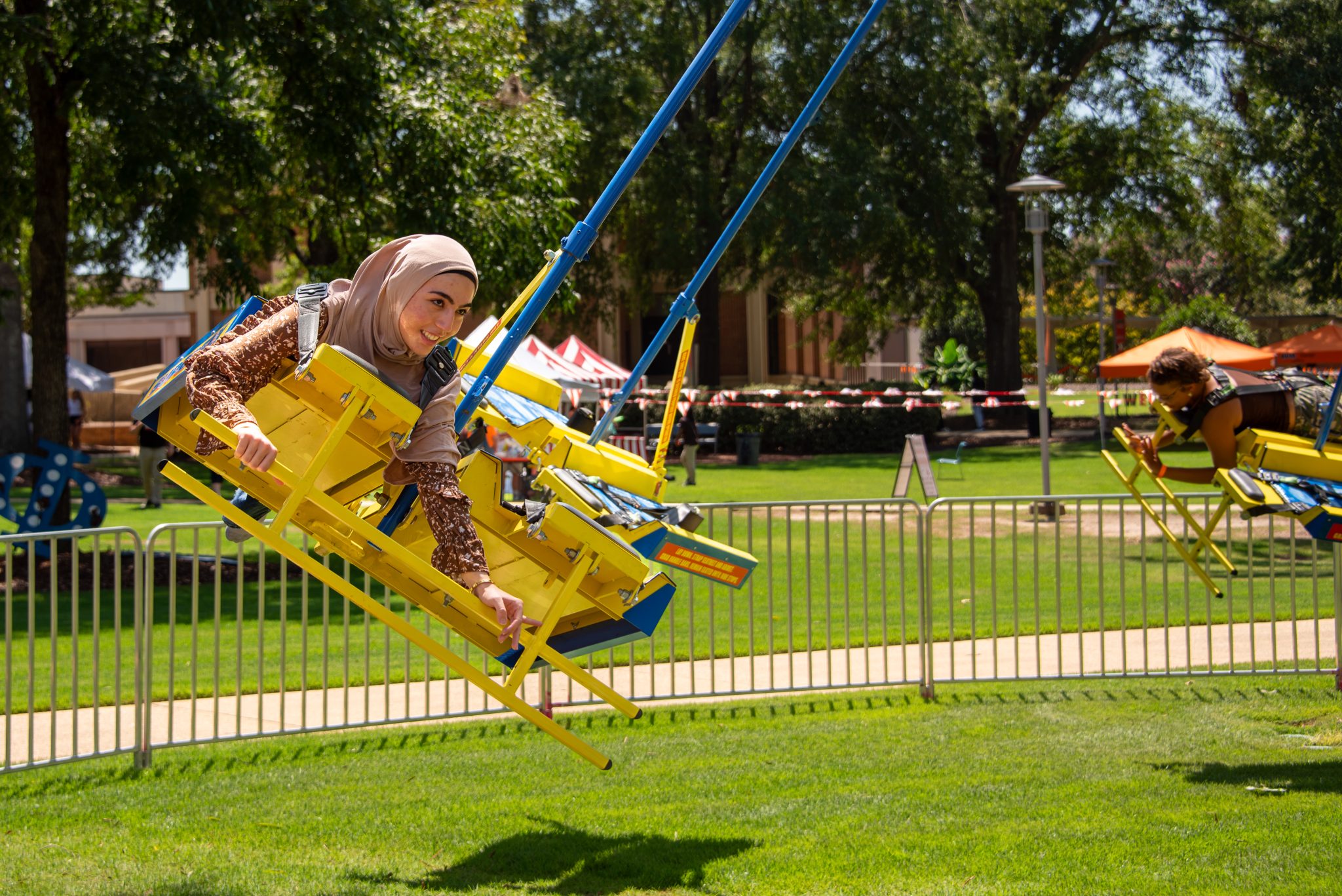 A student enjoys a swing ride during a campus festival on the Auburn University at Montgomery quad under sunny skies.