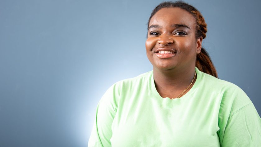 Auburn University At Montgomery Student Smiling In A Light Green Shirt, Studio Portrait On Blue Background