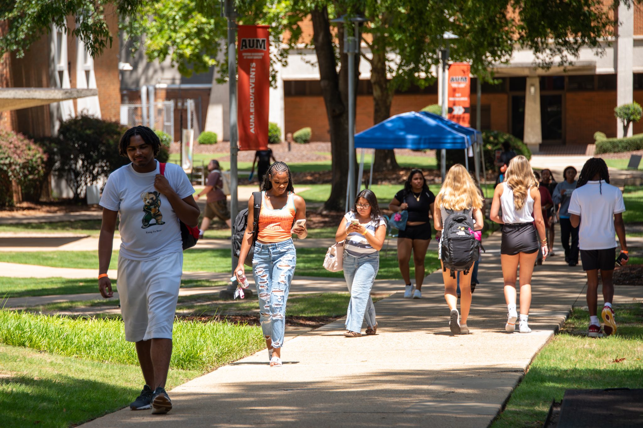 Auburn University at Montgomery students walk across the campus quad under AUM banners on a sunny day