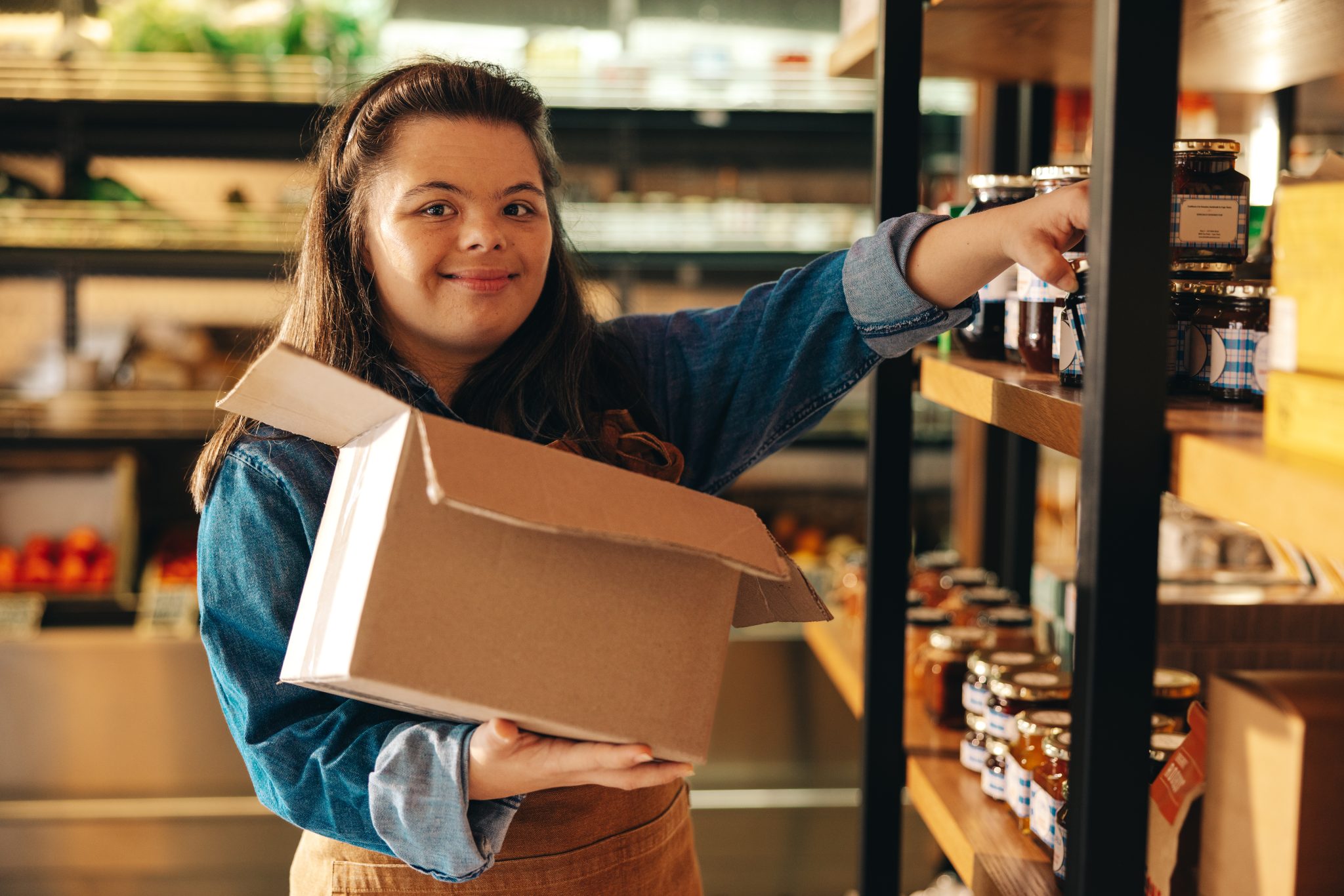 Auburn University at Montgomery student stocks jars on store shelves, holding a box during retail work experience