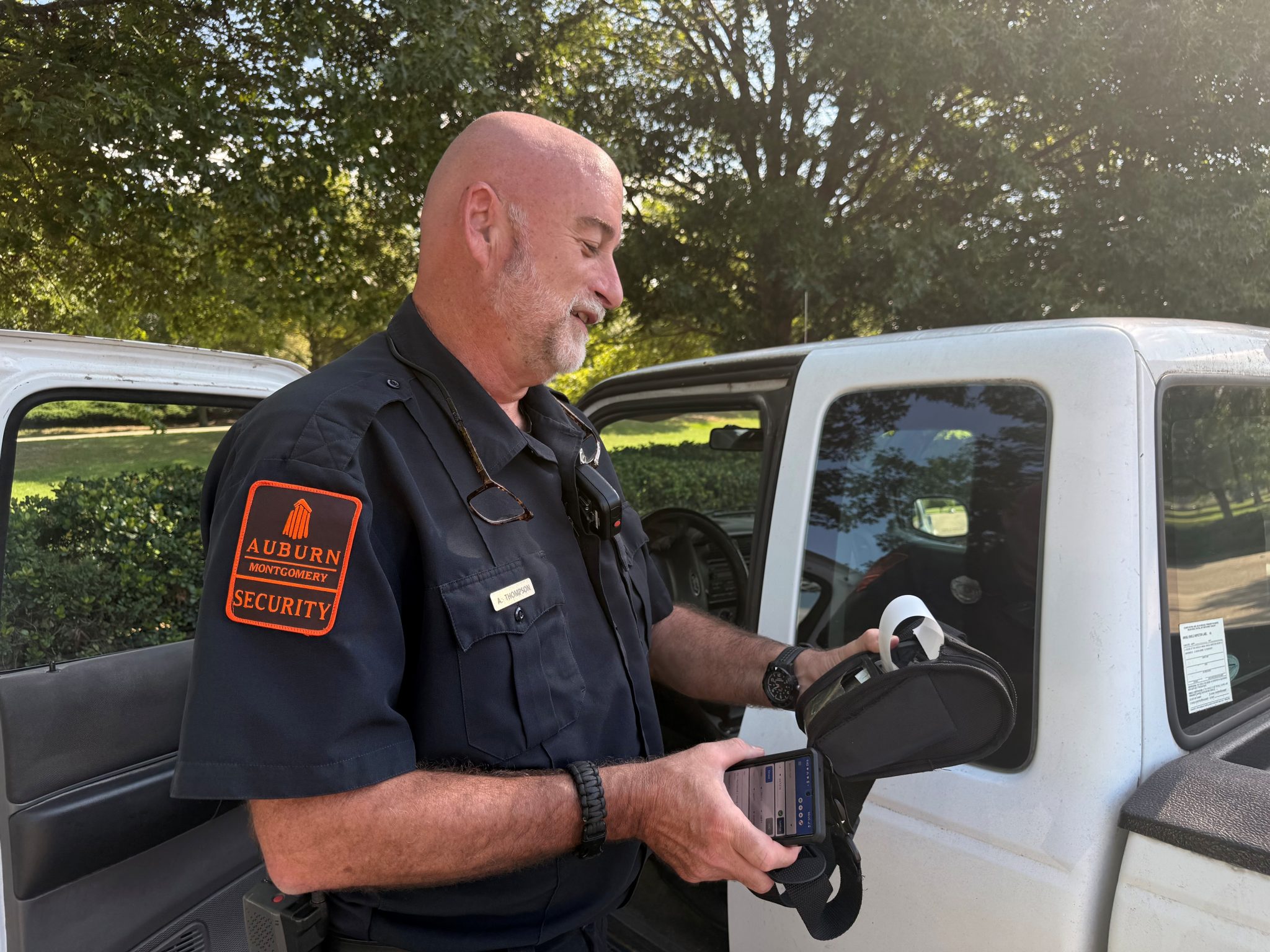 Auburn University at Montgomery campus security officer using ticketing device beside patrol vehicle outdoors.