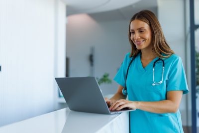 Auburn University at Montgomery nursing student in scrubs using a laptop with stethoscope in a clinic.
