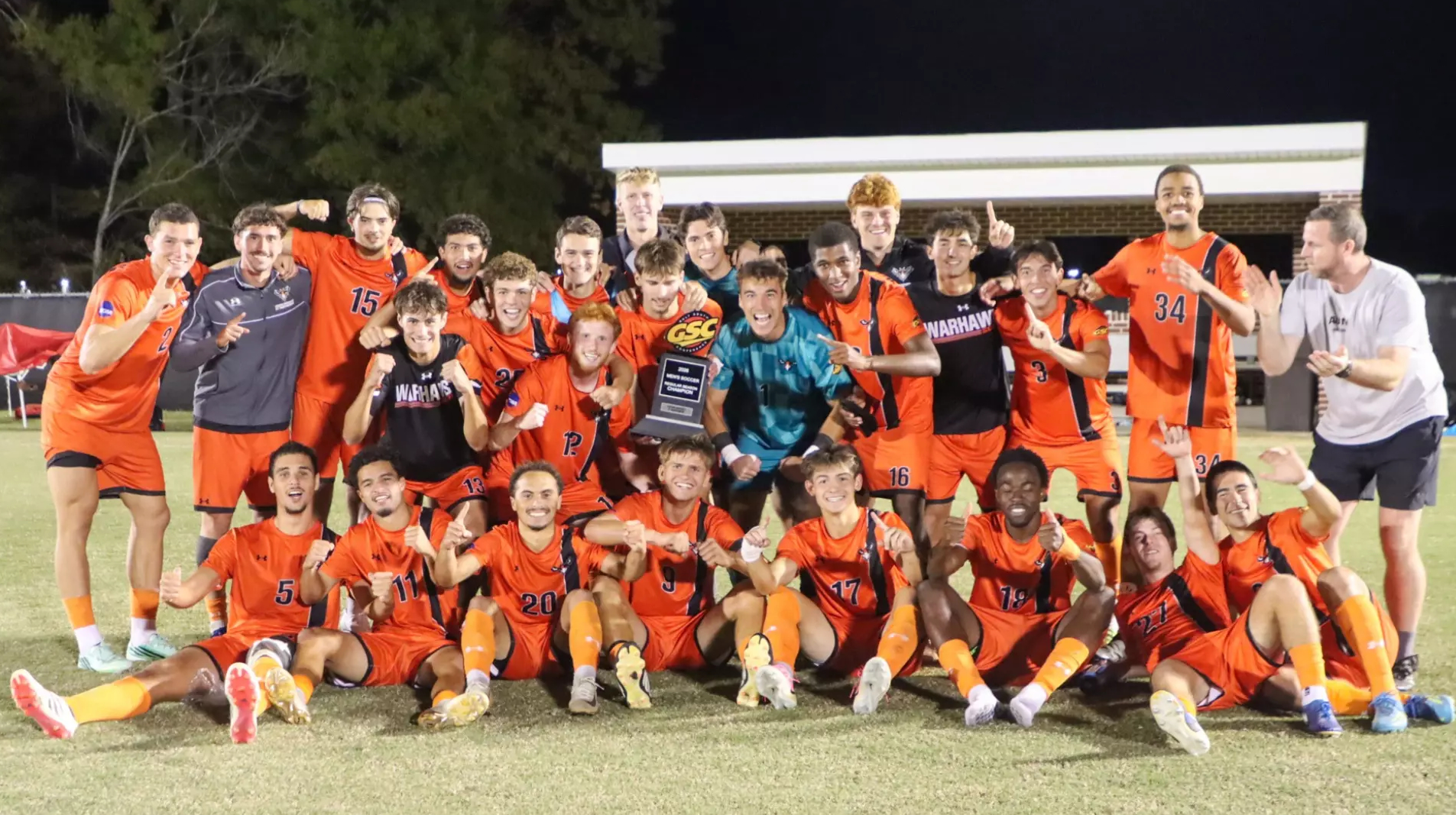 Auburn University at Montgomery Warhawks men's soccer celebrates GSC title with trophy on the field at night.