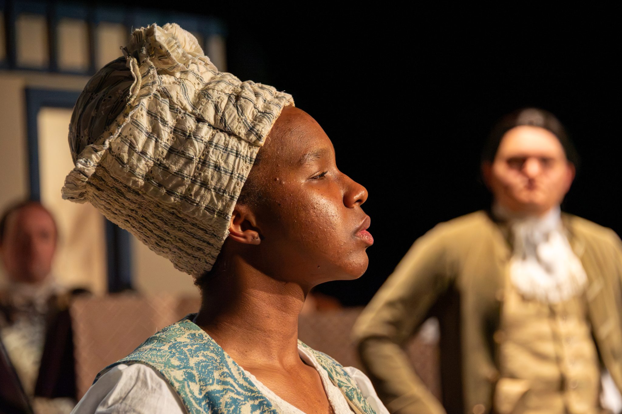 Auburn University at Montgomery theatre scene with a person in colonial costume, side profile, actors blurred.