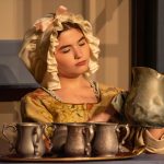 Auburn University at Montgomery theatre: a person in period costume polishing a pewter pitcher and mugs on stage