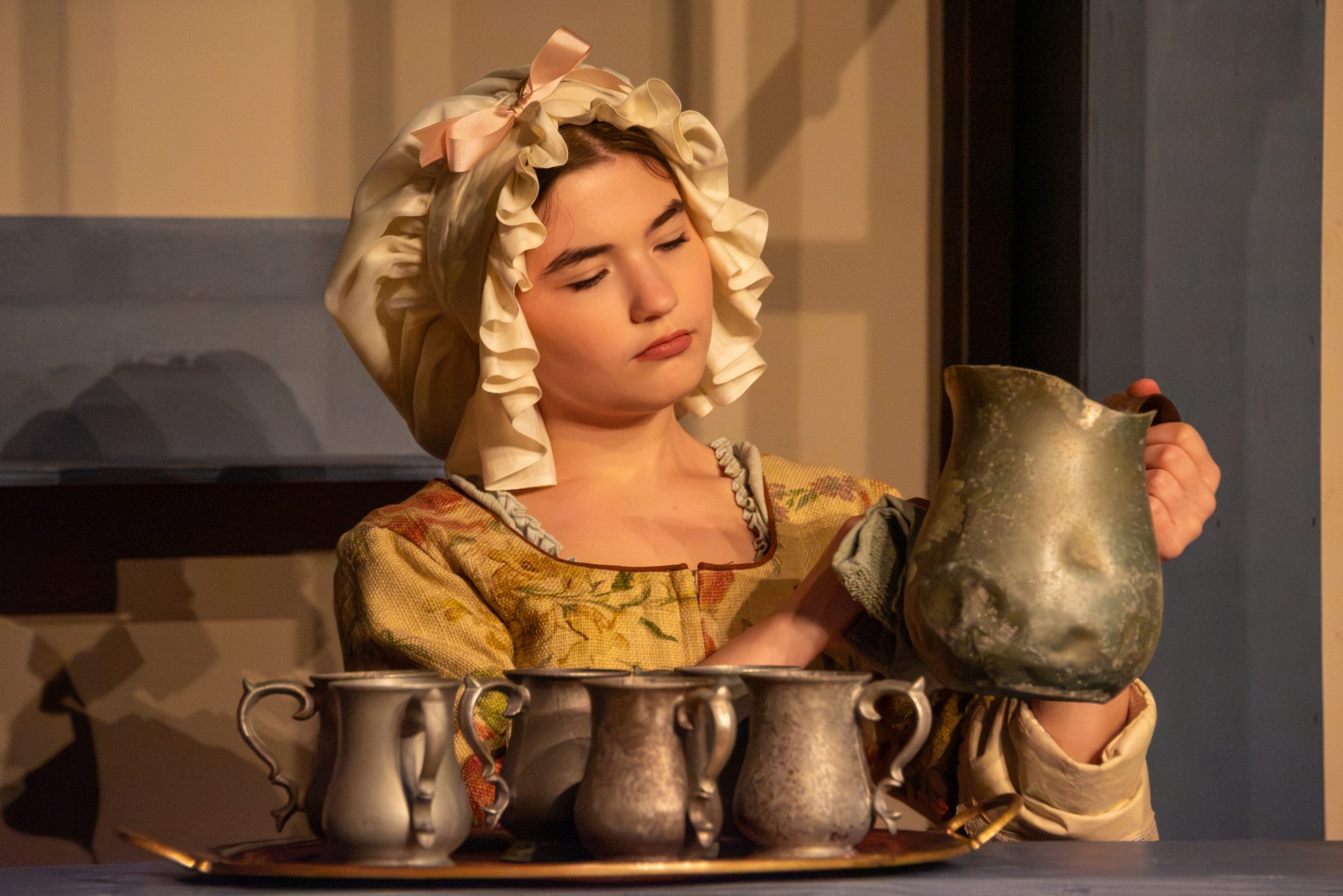 Auburn University at Montgomery theatre: a person in period costume polishing a pewter pitcher and mugs on stage